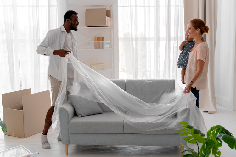 A couple laying a plastic cover over couch to protect it in storage