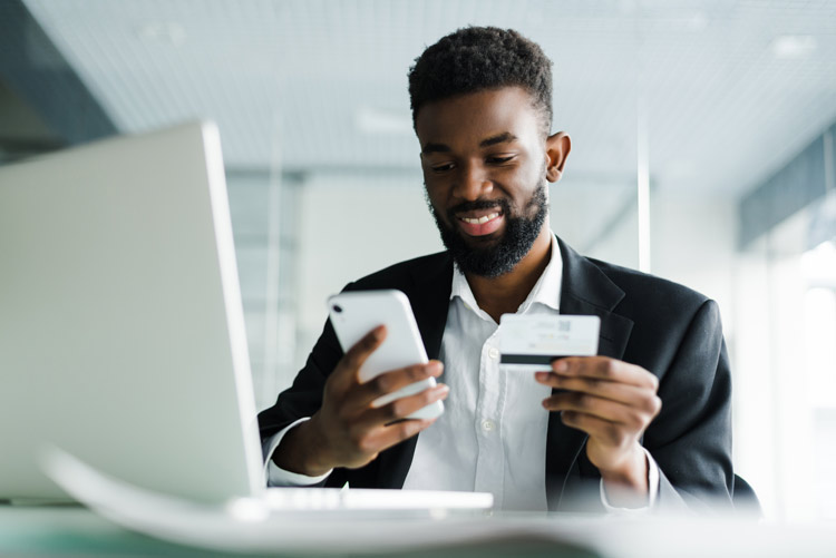 a man using his smart phone and computer to pay off credit card debt.