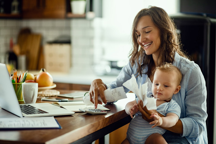 Mother sitting with baby in kitchen while going through receipts.